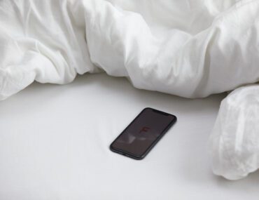 Erotik-Hörbücher: Diese 3 Kurzgeschichten prickeln garantiert  Handy mit femtasy Logo auf einem Bett