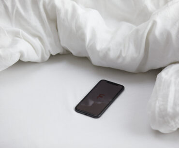 Erotik-Hörbücher: Diese 3 Kurzgeschichten prickeln garantiert  Handy mit femtasy Logo auf einem Bett