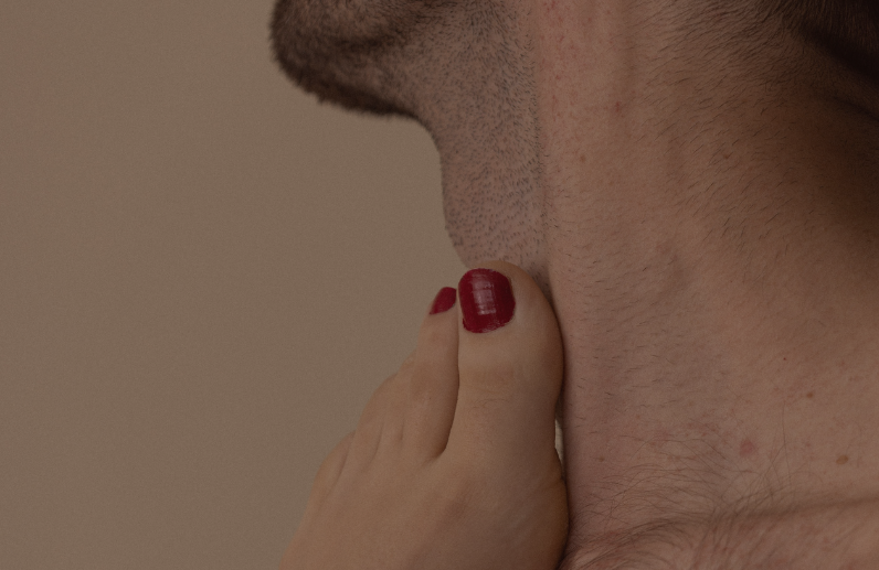Ein Fuß ist an den Hals einer männlich gelesenen Person gelegt.